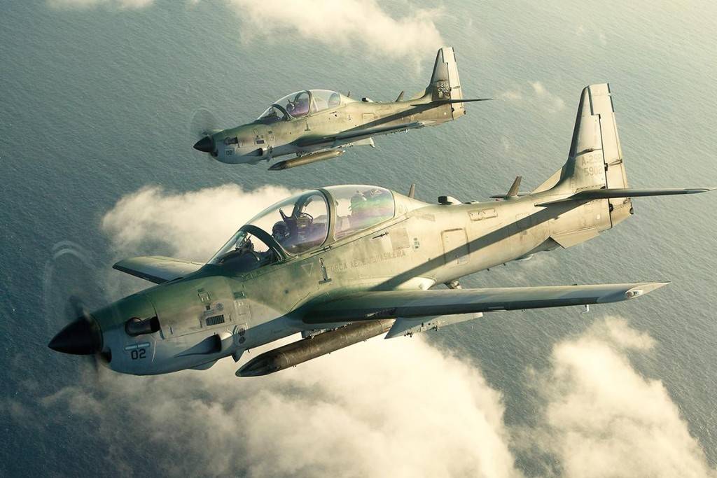 Dois aviões militares do modelo Super Tucano da Embraer sobrevoam o mar.