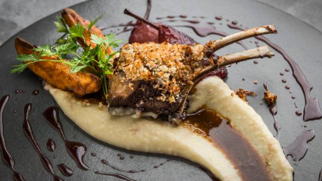 O carré de cordeiro com crosta de pão é guarnecido de purê de batata com pedacinhos de maçã crua, molho demi-glace, batata rústica e pera ao Barolo, finalizado com o molho de vinho que banha a fruta. Foto: Letícia Akemi/Bom Gourmet