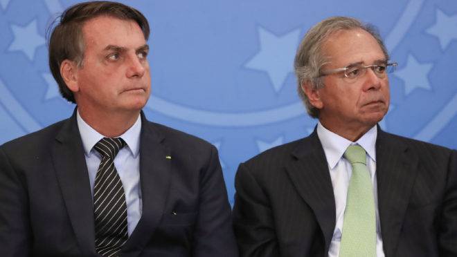 O presidente Jair Bolsonaro sentado ao lado do ministro da Economia, Paulo Guedes.