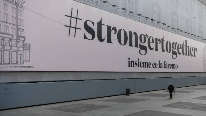 Em Milão, na Itália, uma mulher passa por um outdoor gigante com a seguinte mensagem: “juntos somos mais fortes”