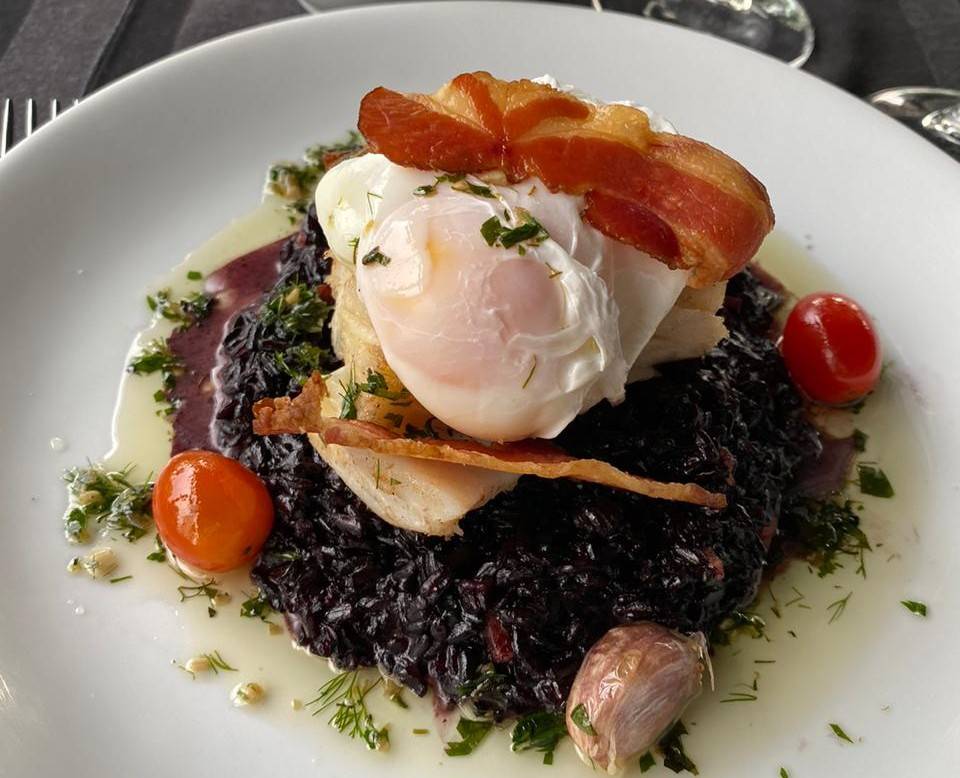 Lombo de bacalhau, arroz negro, ovo pochê, bacon e azeite de ervas frescas do Mukeka. Foto: Divulgação Lombo de bacalhau, arroz negro, ovo pochê, bacon e azeite de ervas frescas do Mukeka. Foto: Divulgação