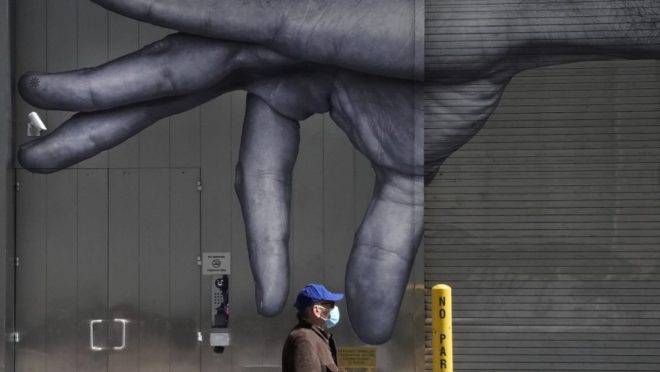 Homem usando máscara passa por mural em Nova York, 22 de abril de 2020. O novo coronavírus matou mais americanos em um mês do que a gripe comum mata em média por ano
