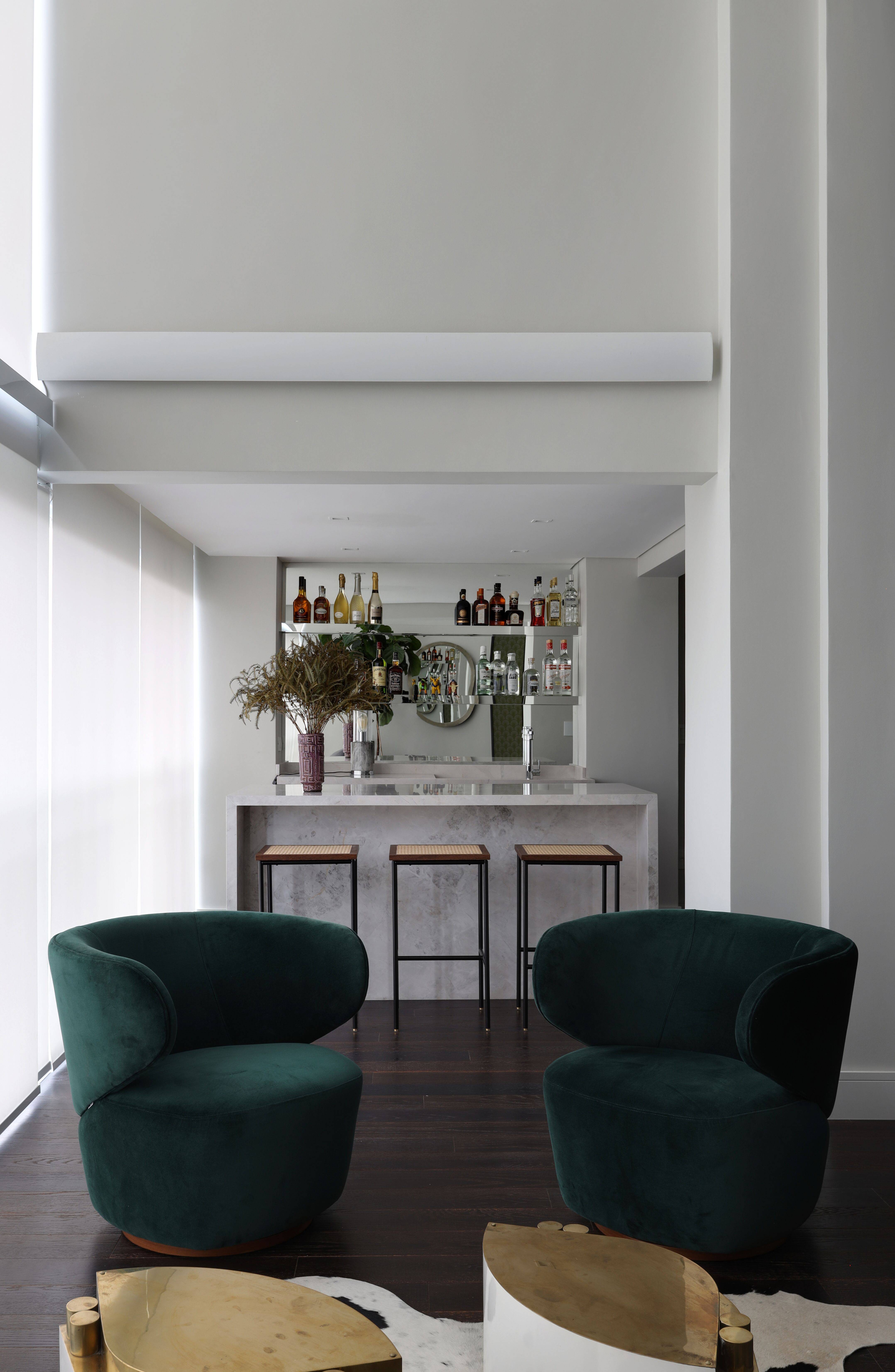 Um generoso bar foi montado com bancada de mármore e prateleiras espelhadas, em um lounge despojado com poltrona e mesas de apoio. Um generoso bar foi montado com bancada de mármore e prateleiras espelhadas, em um lounge despojado com poltrona e mesas de apoio.