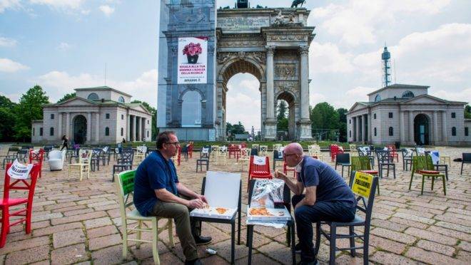 Donos de restaurante almoçam entre mesas vazias em frente ao monumento Arco della Pace, na Piazza Sempione, em Milão, em protesto contra o fechamento prolongado de seus negócios, no dia 6 de maio.