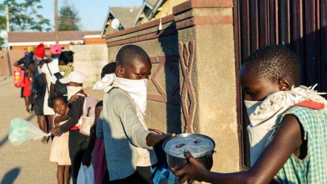 Pessoas formam fila para receber refeição doada por moradora de Chitungwizaon, Zimbábue, durante lockdown imposto pelo governo para conter o coronavírus, 5 de maio de 2020. Com ajuda de voluntários, Samantha Murozoki serve mais de 100 refeições por dia de sua casa a pessoas carentes cuja renda foi reduzida pelo fechamento dos negócios durante o lockdown
