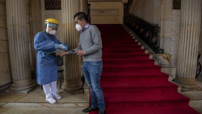 Profissional da saúde mede temperatura de visitante no Congresso Nacional da Colômbia, em Bogotá.
