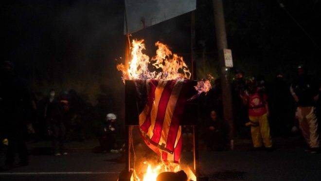 Bandeira norte-americana é incendiada por manifestantes em Portland.