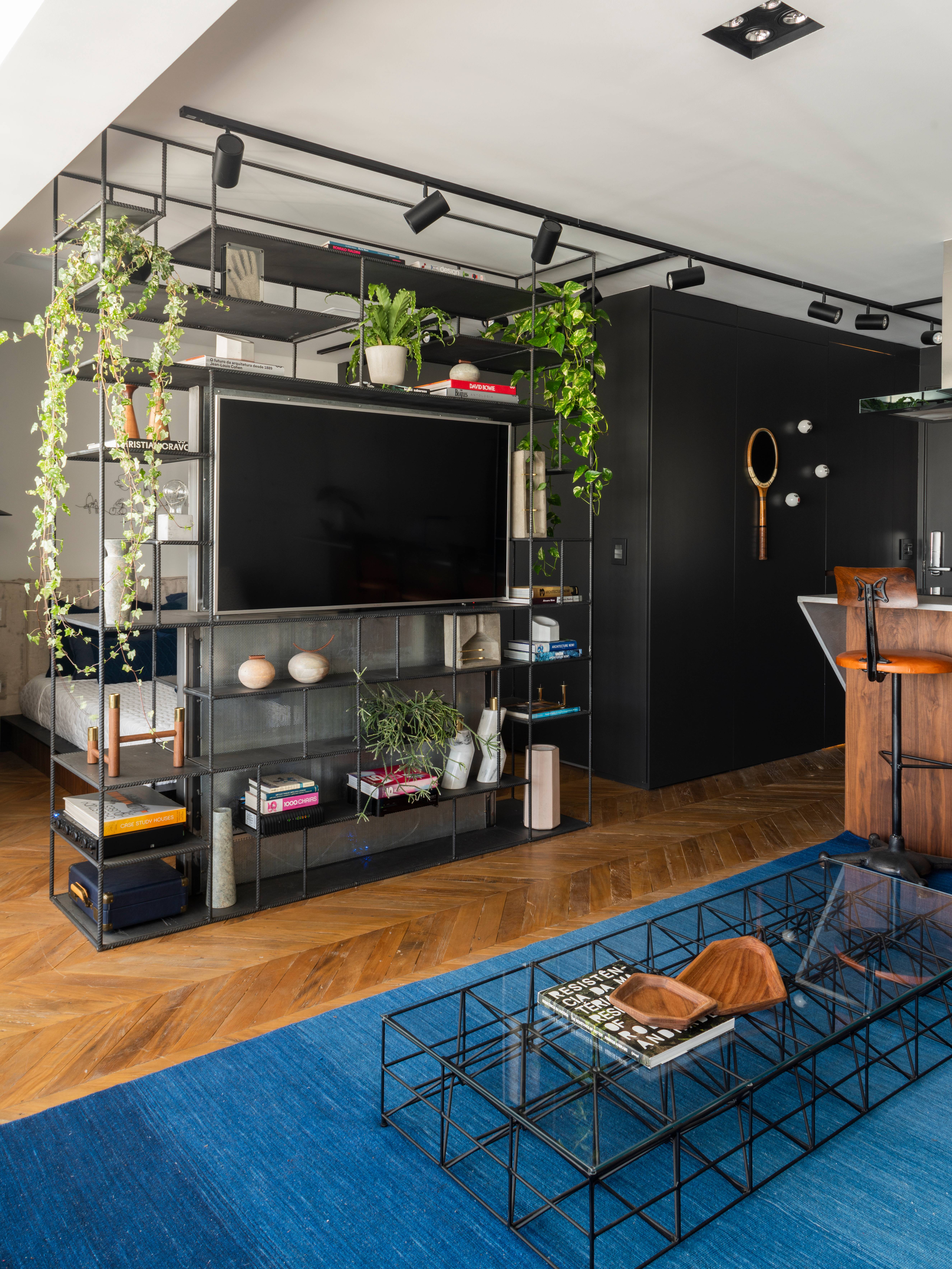 Em metal, estante delimita e integra os ambientes, servindo ao living e ao dormitório no projeto da Rua 141 e de Rafael Zalc. Foto: Divulgação Em metal, estante delimita e integra os ambientes, servindo ao living e ao dormitório no projeto da Rua 141 e de Rafael Zalc. Foto: Divulgação