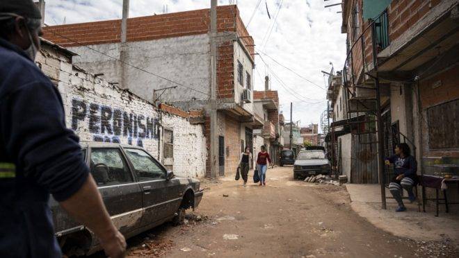 Mulher caminha em favela de Buenos Aires. No Muro, pichação referente ao Peronismo, legado do presidente Juan Perón, morto em 1974.