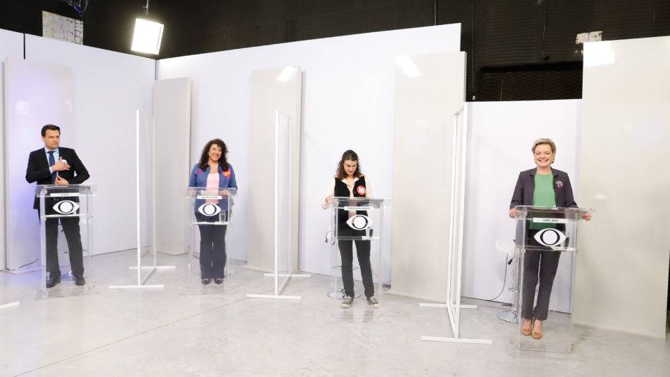 Imagem em plano aberto mostra quatro candidatos, lado a lado, contra fundo de painéis claros na BandTV