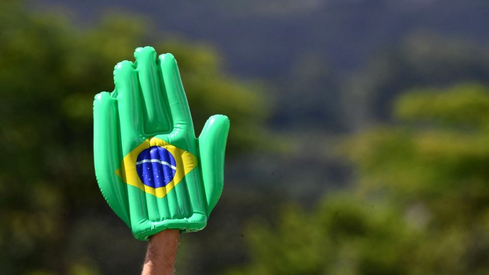 A peste para além do bem e do mal A supporter of Brazilian President Jair Bolsonaro holds up an inflatable hand depicting Brazil’s flag on his birthday, outside the lawns of the Alvorada Palace, in Brasilia, on March 21, 2021. (Photo by EVARISTO SA / AFP)