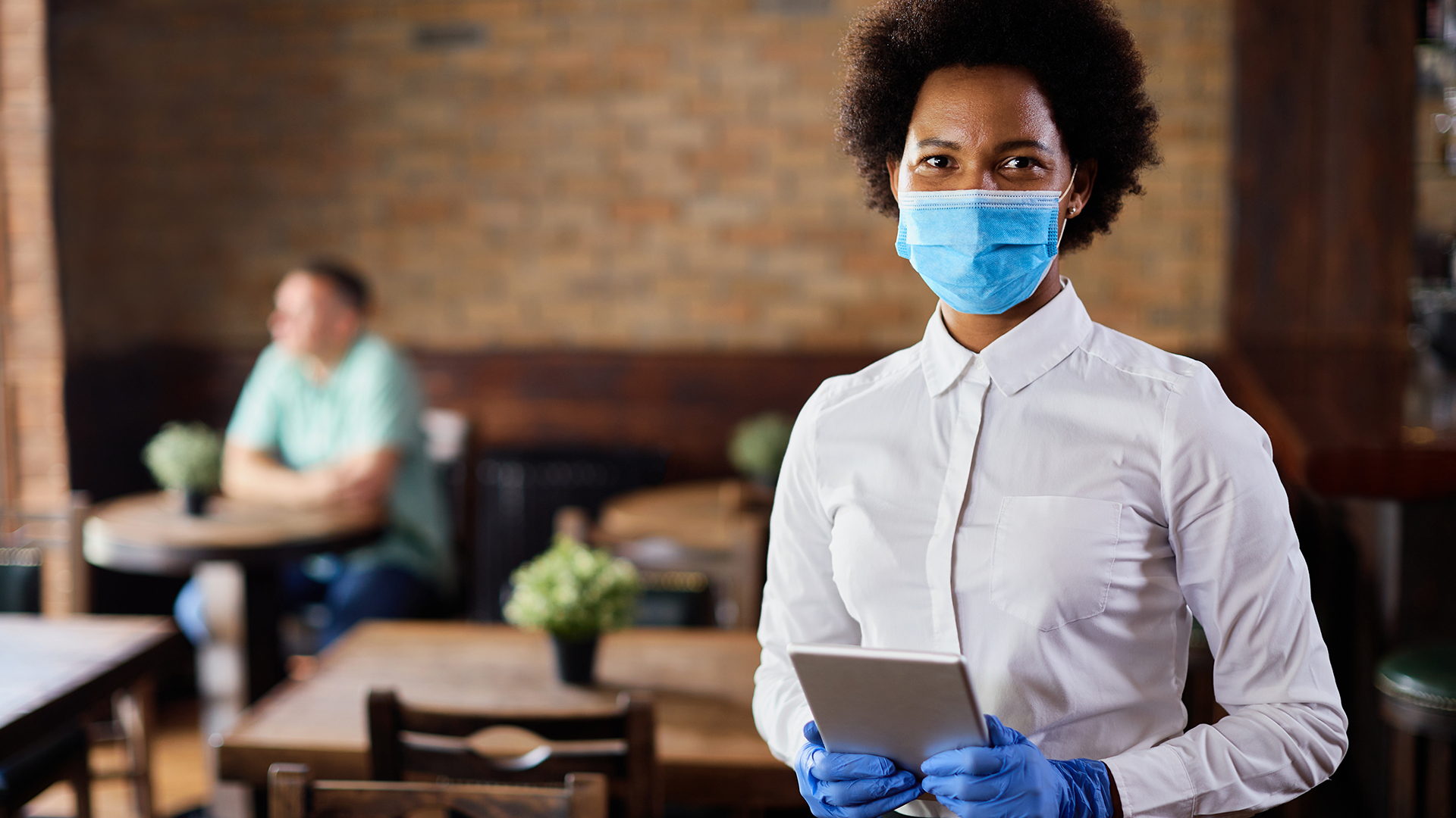 Atendente segurando tablet e usando máscara e luvas devido à pandemia.