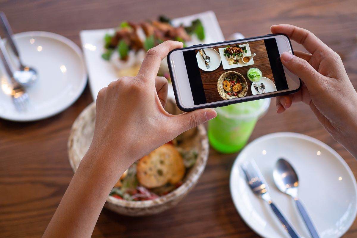 The woman hand is using a mobile phone to take a picture of food on the dining table in the restaurant.  Photography with Mobile Phone Concepts