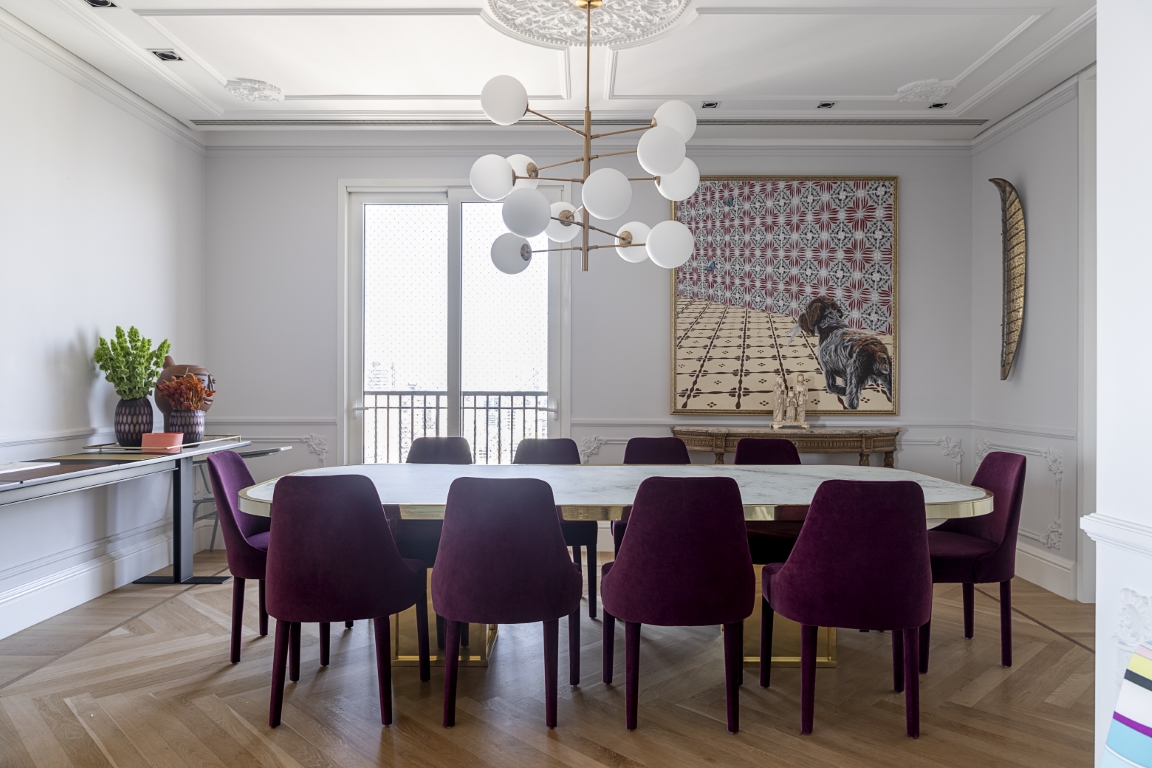 A mesa de jantar foi desenhada pelo escritório Bárbara Jalles Guimarães; as cadeiras de veludo roxo trazem peso ao ambiente. A mesa de jantar foi desenhada pelo escritório Bárbara Jalles Guimarães; as cadeiras de veludo roxo trazem peso ao ambiente.