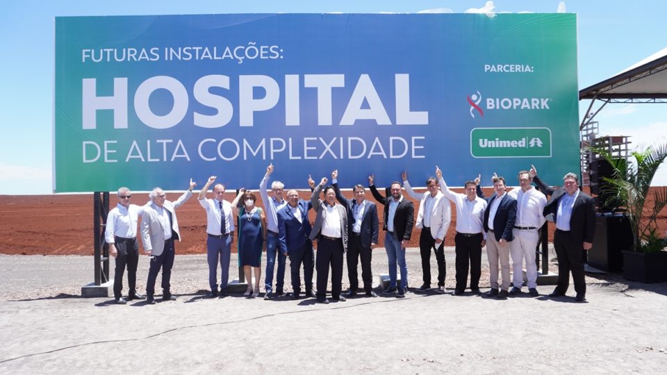 Placa que marca onde o novo hospital da Unimed Paraná será construído, em Toledo, com participantes do evento de lançamento da obra a sua frente.