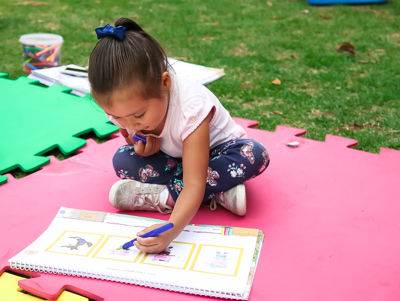 Criança sentada no chão e escrevendo num material didático da Aprende Brasil.