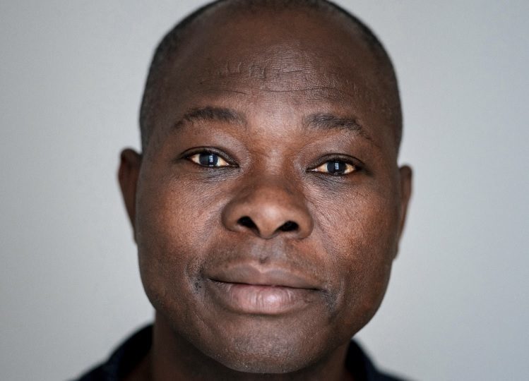 Plano fechado do arquiteto Diébédo Francis Kéré, um homem negro, careca, com olhos amendoados, nariz de base larga e lábios volumosos.
