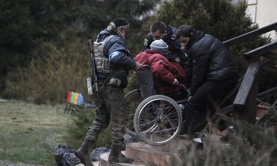 Pessoal da Defesa Territorial ucraniana ajuda a evacuar idosos de um abrigo na cidade de Irpin, neste sábado