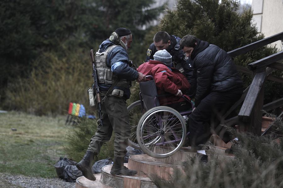 Pessoal da Defesa Territorial ucraniana ajuda a evacuar idosos de um abrigo na cidade de Irpin, neste sábado