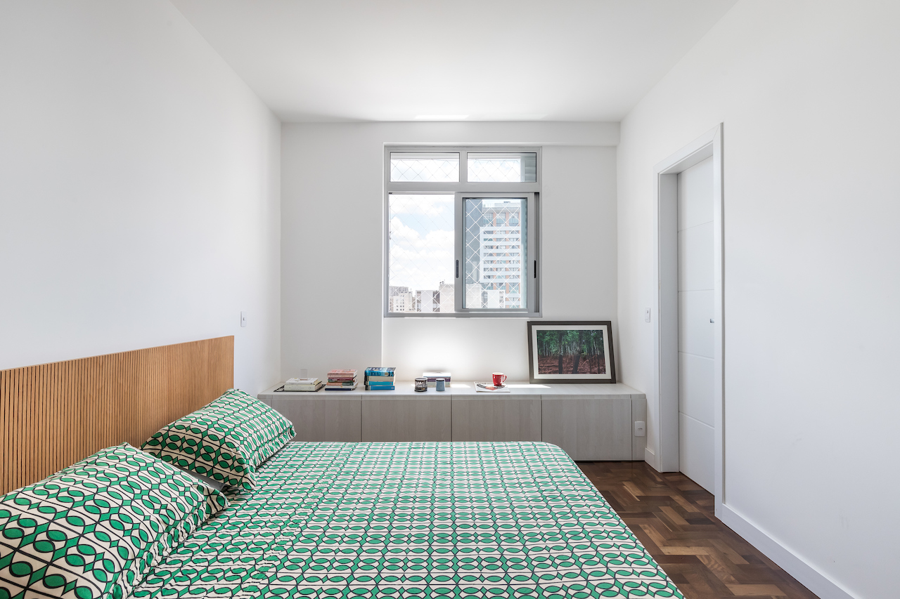 A suíte segue a mesma lógica estética e funcional do restante do apartamento, com pouco mobiliário para protagonizar o espaço. Sob a janela, o banco-gaveteiro organiza as peças da moradora. A suíte segue a mesma lógica estética e funcional do restante do apartamento, com pouco mobiliário para protagonizar o espaço. Sob a janela, o banco-gaveteiro organiza as peças da moradora.