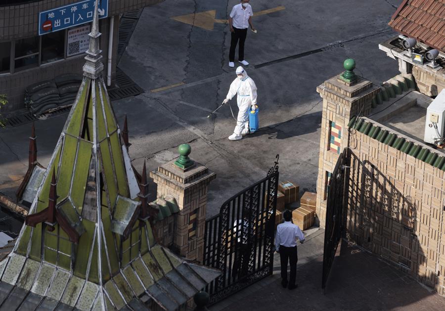 Homem com equipamento de proteção desinfeta uma rua em Xangai, neste sábado