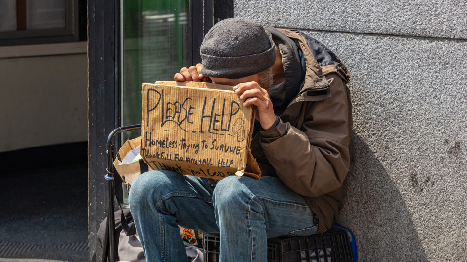 Homem em situação de rua pede ajuda com cartaz de papelão em Manhattan, Nova York