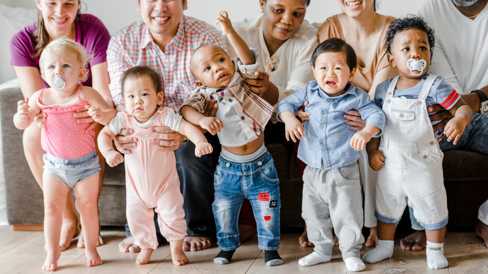 Bebês de diversas cores posam juntos para foto com seus pais