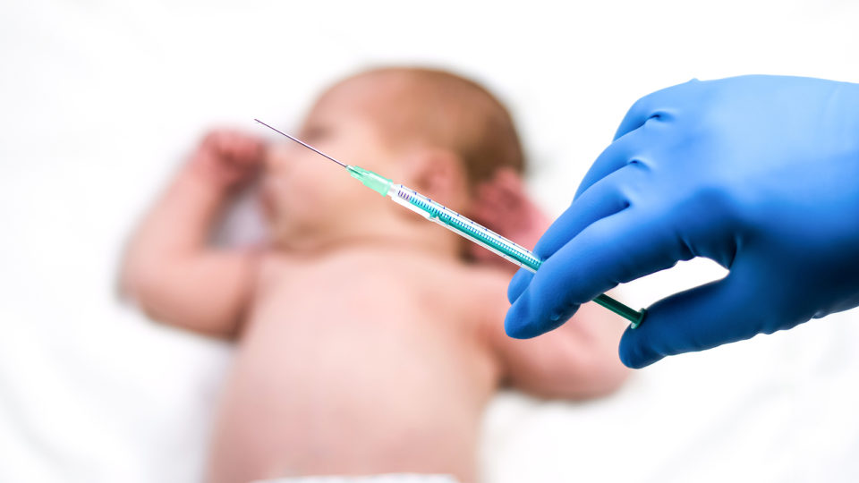 Seringa em mão de médico com um bebê ao fundo