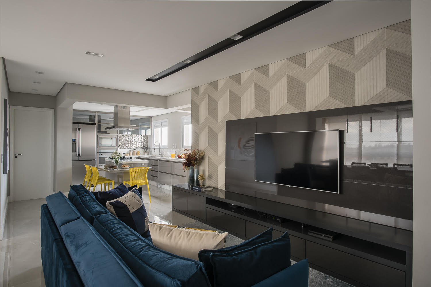 Nesta sala projetada por PB Arquitetura, o painel e rack do ambiente são da tonalidade do televisor, que ajudam a criar uma unidade ao mesmo tempo em que escondem a fiação dos eletrodomésticos