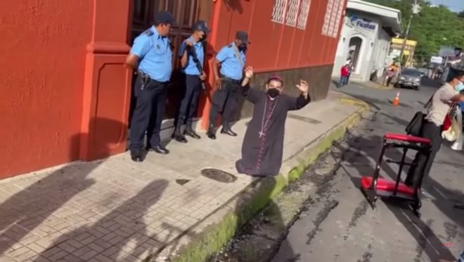 O monsenhor Rolando Álvarez, ajoelhado em frente à Diocese de Matagalpa, ao ser impedido de fazer uma procissão para pedir o fim da repressão à Igreja na Nicarágua.