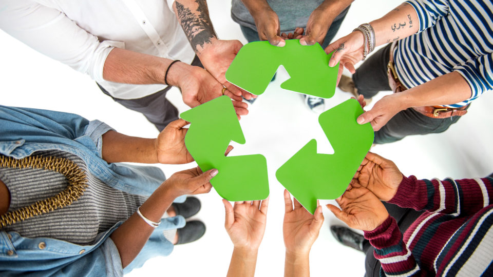 Grupo de pessoas segurando símbolo da reciclagem.