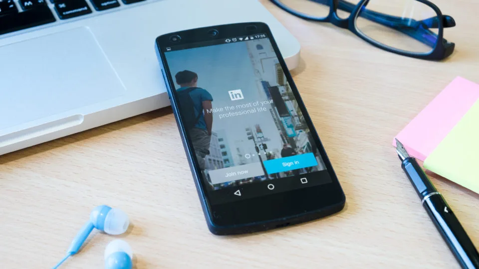 Mesa de trabalho com celular com LinkedIn aberto