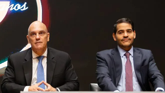 Imagem de Jorge Messias em foto oficial, ao lado de Flávio Dino e Alexandre de Moraes, com sobreposição de algemas, câmeras apagadas e a bandeira do Brasil invertida, simbolizando