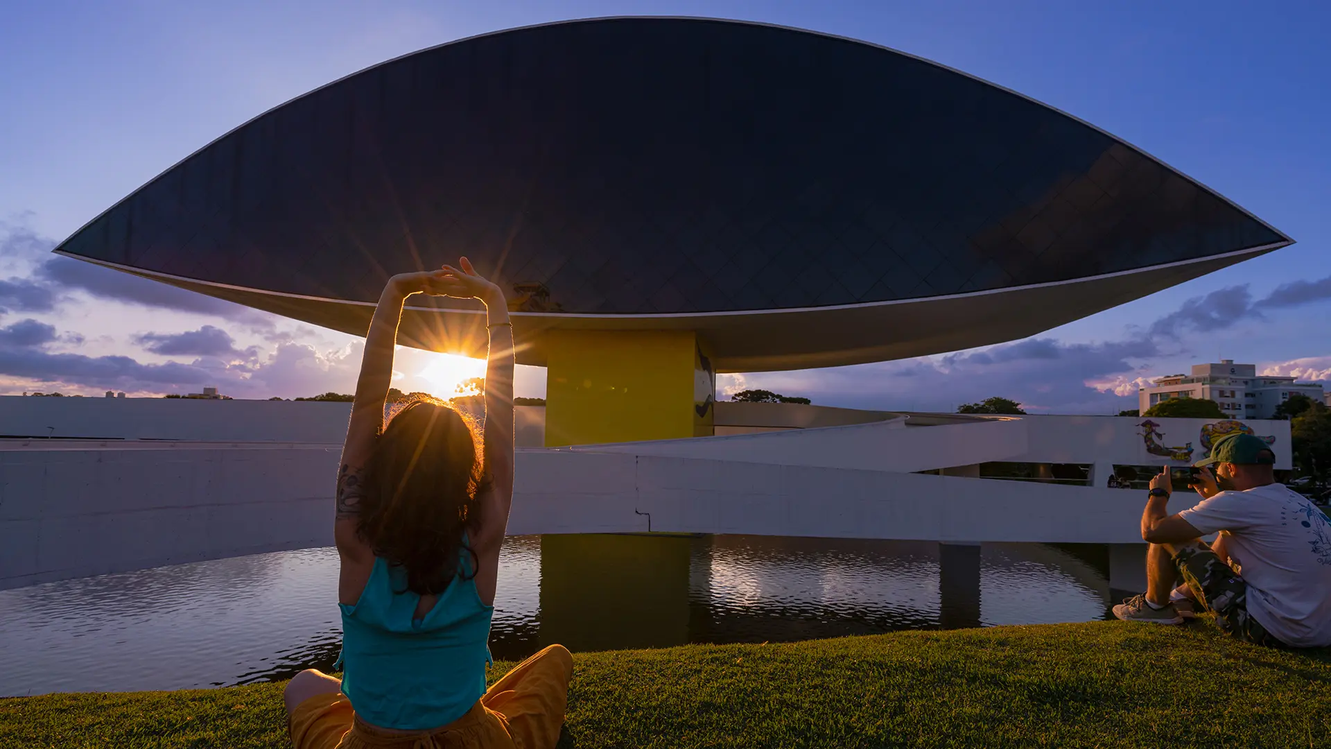 Homem e mulher sentados curtindo o entardecer nos jardins do Museu Oscar Niemeyer (MON), em Curitiba.