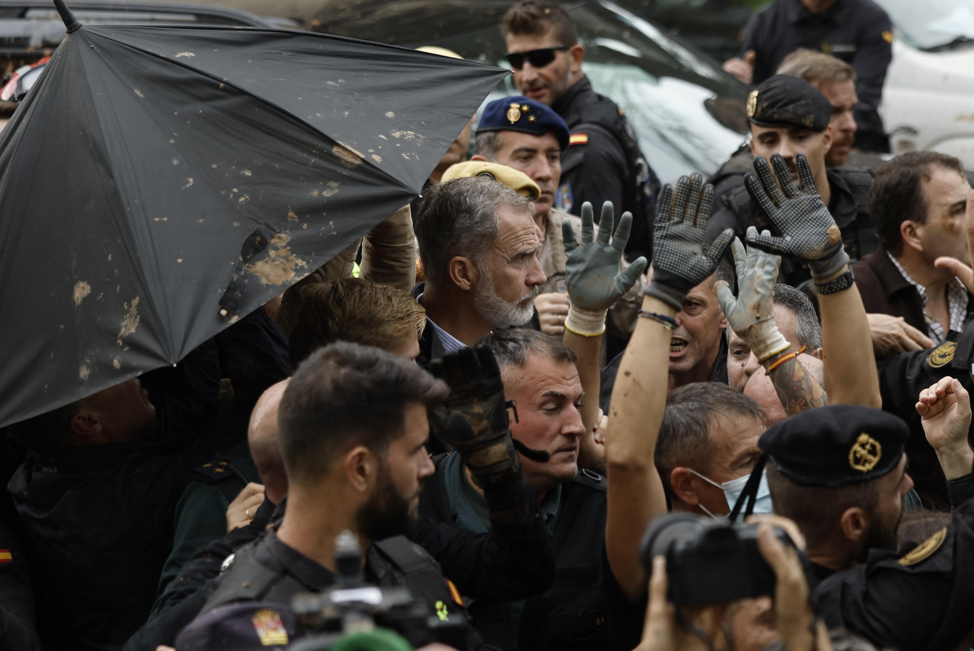 O rei Felipe, ao centro, é protegido da lama arremessada por um guarda-chuva