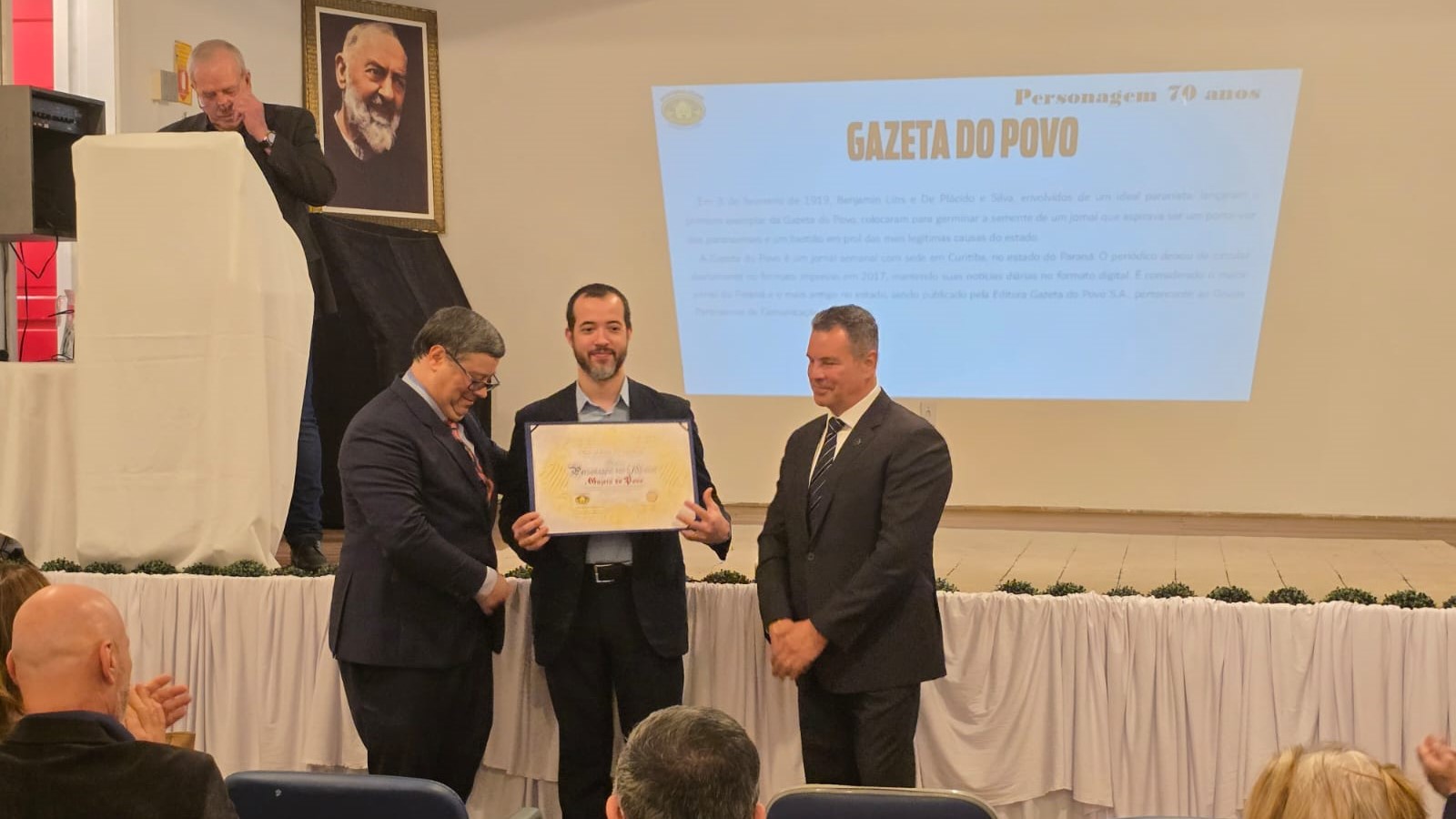 Gazeta do Povo, representada por Jônatas Dias Lima, coordenador das editorias de Opinião e Ideias, recebe título &#8220;Personagem dos 70 Anos&#8221;; à direita o juiz Haroldo Demarchi Mendes e à esquerda Rafael Êrico Kalluf Pussoli, engenheiro civil e presidente voluntário da Casa dos Pobres São João Batista.