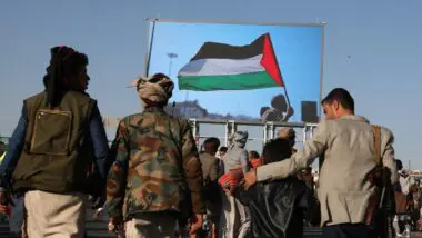 Apoiadores Houthis passam por um outdoor digital com um homem acenando uma bandeira palestina durante um protesto anti-EUA e anti-Israel em Sana'a, Iêmen, 15 de novembro de 2024.