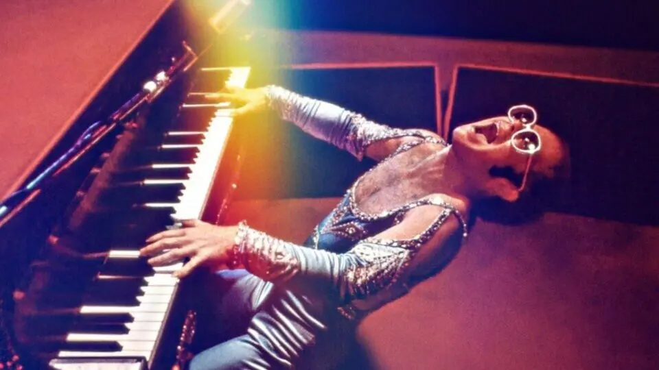 O cantor, compositor e pianista inglês Elton John com as roupas e óculos chamativos que marcaram sua carreira