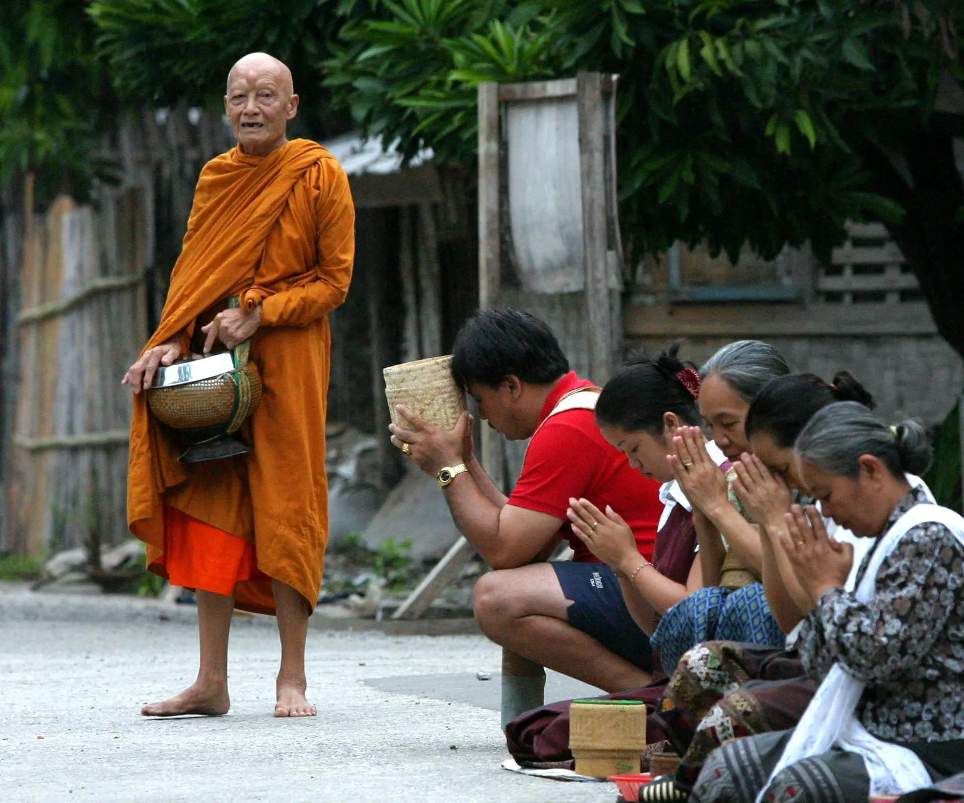 Um monge faz orações por alguns moradores de Luang Prabang depois que eles deram comida a alguns dos 800 monges da cidade, logo após o nascer do sol, 13 de setembro de 2003. Antiga capital real do Laos, Luang Prabang é o maior cartão de visita turístico para o Laos. A cidade foi declarada patrimônio mundial da UNESCO em 1995.