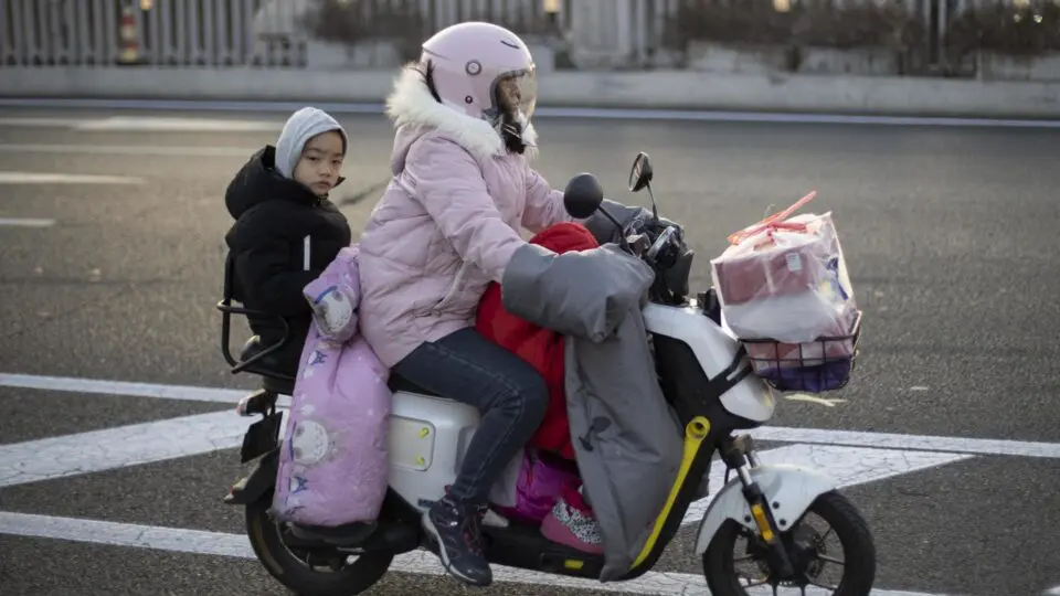 Mulher chinesa dirige uma moto elétrica carregando duas crianças em Pequim, China, 17 de janeiro de 2025