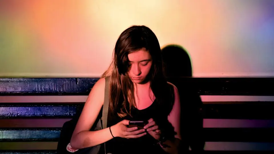 Menina sentada em um banco mexendo na tela do seu celular.