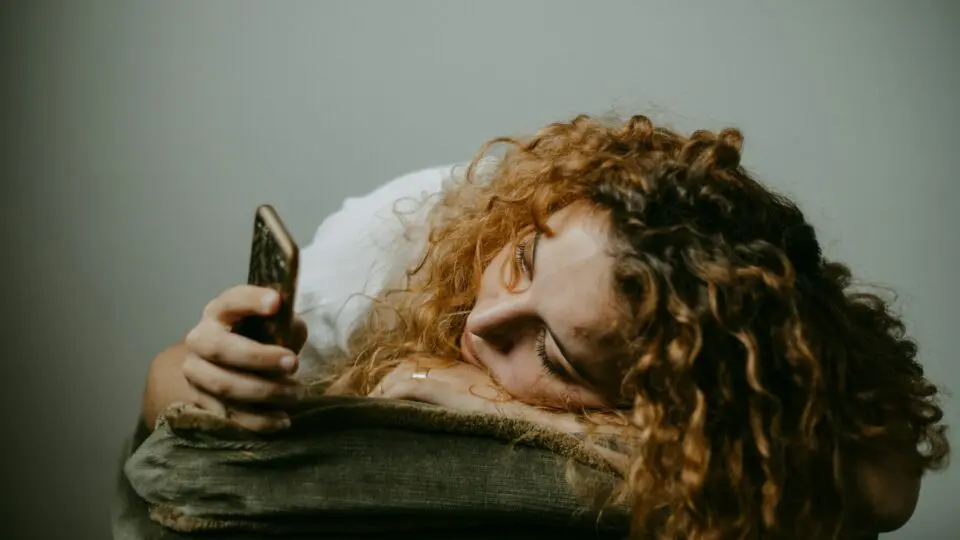 Menina deitada sobre a bolsa e com celular na mão.