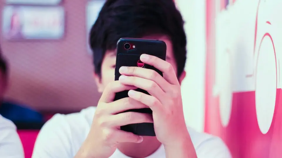Adolescente com um celular na mão. Ele está olhando para tela.