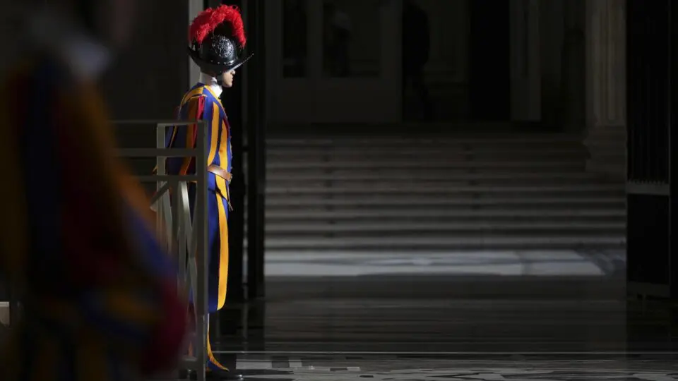 Soldado da Guarda Suíça parado, no Vaticano. Ele usa as vestes tradicionais, azul, amarela e vermelha.