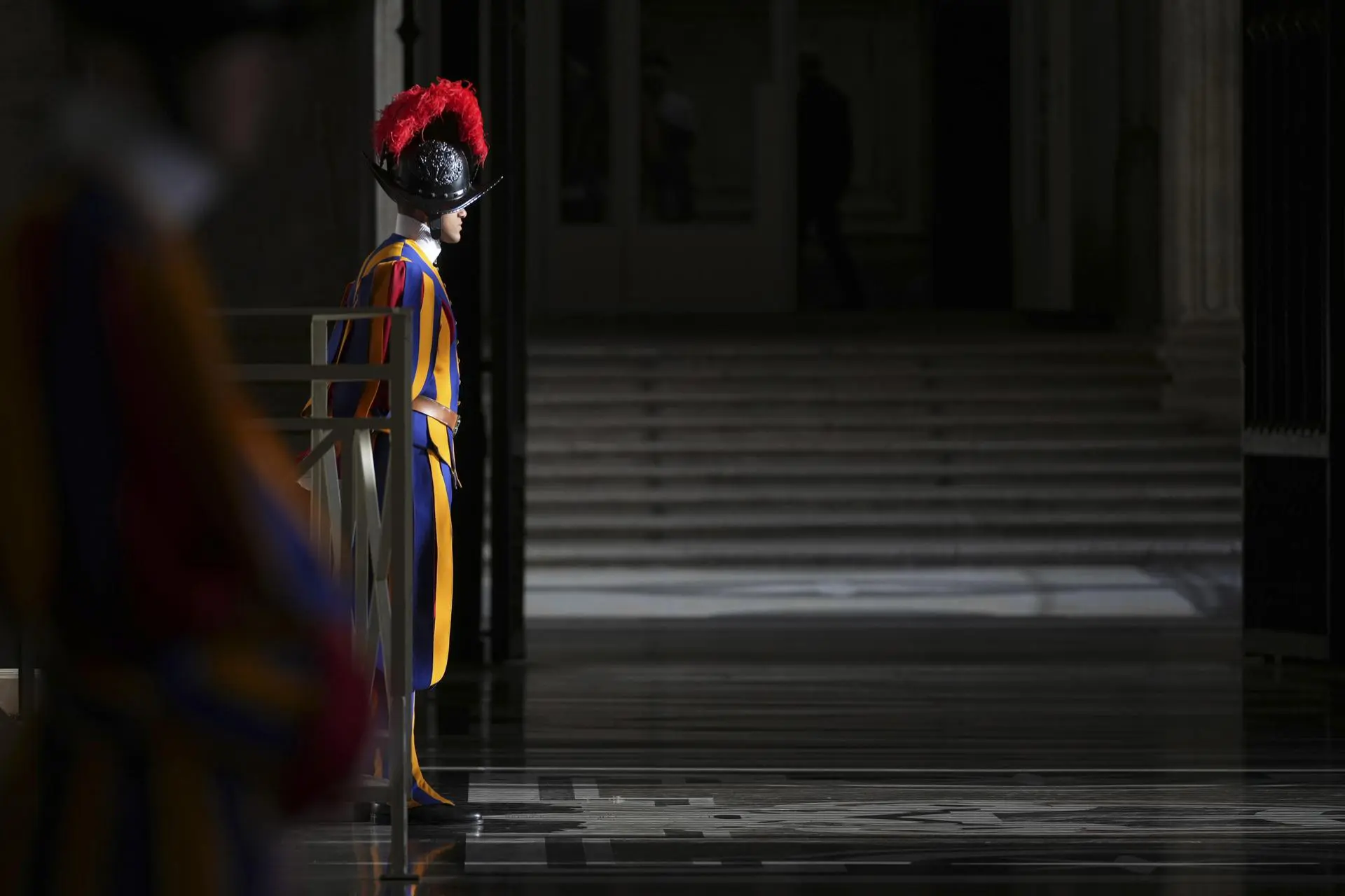 Soldado da Guarda Suíça parado, no Vaticano. Ele usa as vestes tradicionais, azul, amarela e vermelha.