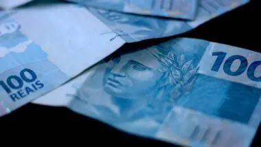 Cédulas de cem reais no fundo preto.