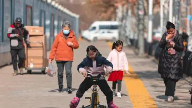 Pessoas caminham em frente ao Mercado de Frutos do Mar de Huanan, fechado e cercado, em Wuhan, província de Hubei, China, 20 de janeiro de 2025. O mercado de frutos do mar de Huanan, suspeito de ser uma fonte potencial do vírus, permanece fechado, com guardas de segurança ainda posicionados do lado de fora. A OMS estima quase 800 milhões de infecções e sete milhões de mortes, embora os números variem.