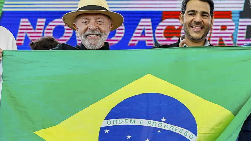 Lula e o ministro da AGU, Jorge Messias, posam com uma banderia do Brasil em evento no ES