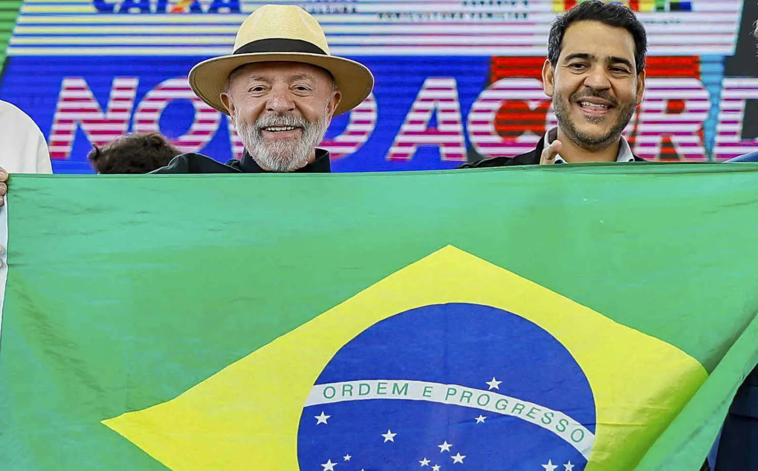 Lula e o ministro da AGU, Jorge Messias, posam com uma banderia do Brasil em evento no ES