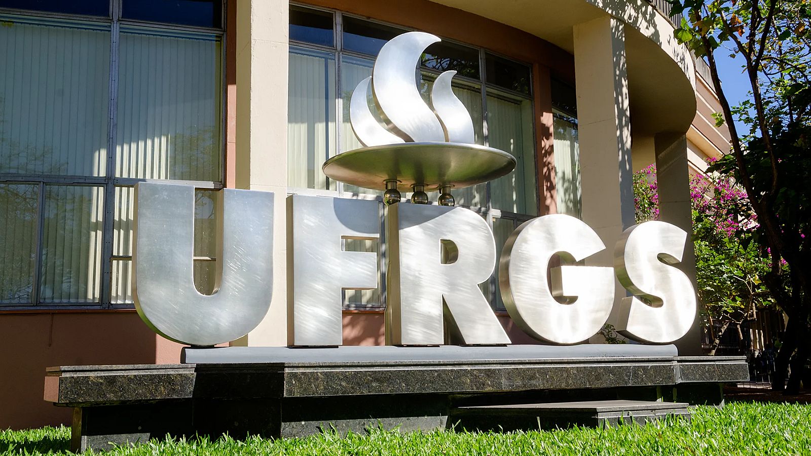 Logo da UFRGS diante do edifício da reitoria da universidade.